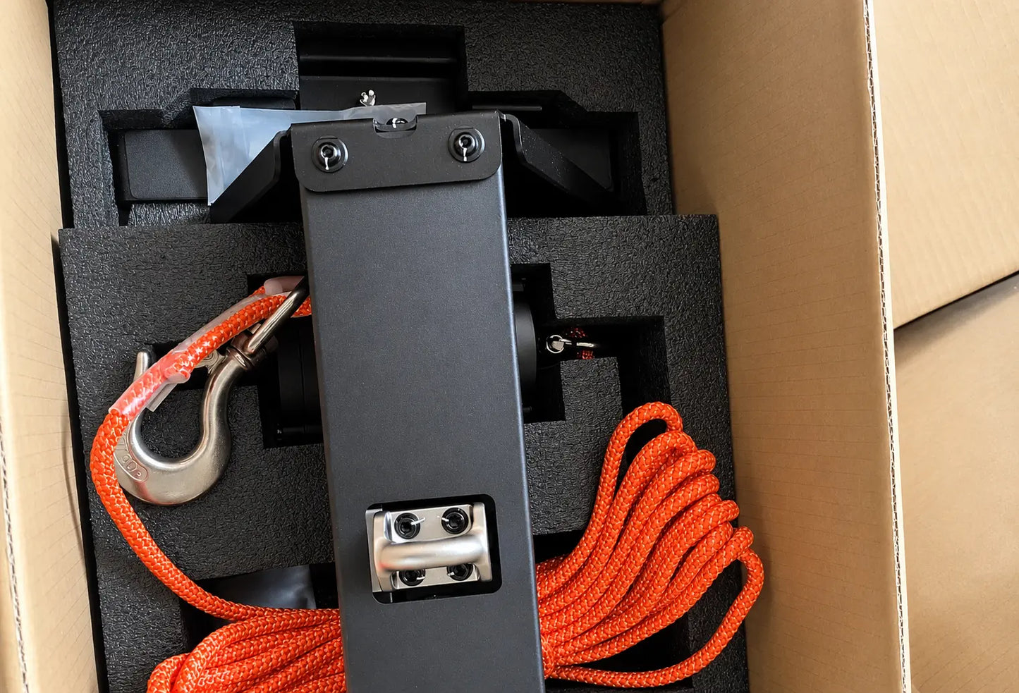 Black mounting plate with hook and orange braided cable, packed in foam tray