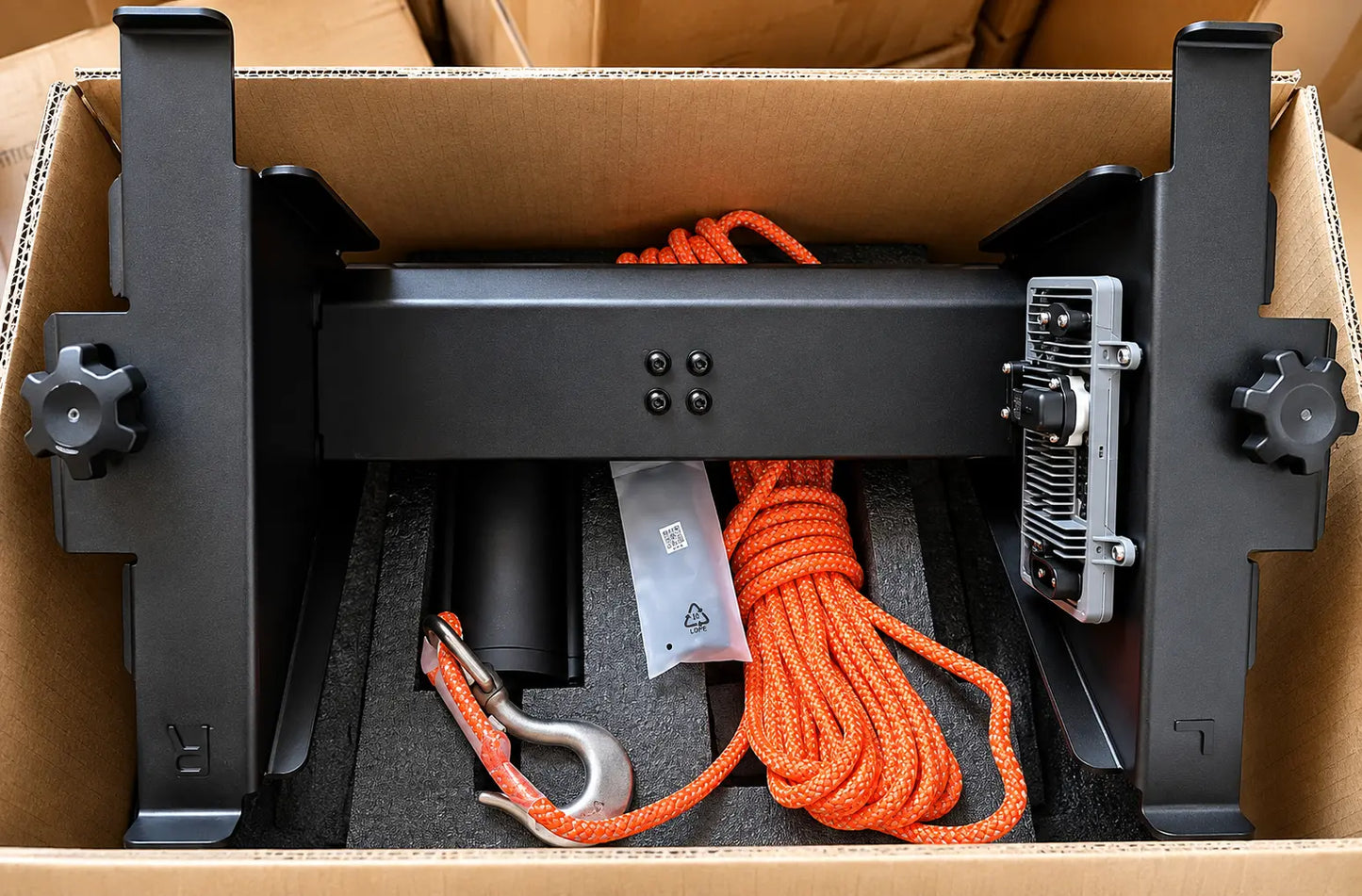 OEM lifting system in packaging: black frame, orange braided cable, cable strain relief